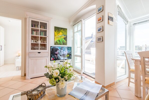 A modern living room with a television, a bookshelf, a dining area, and a large window with a city view.