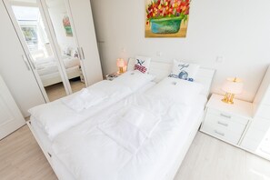 A neatly made double bed with white bedding, a bedside table with a lamp, and a wall painting of tulips.