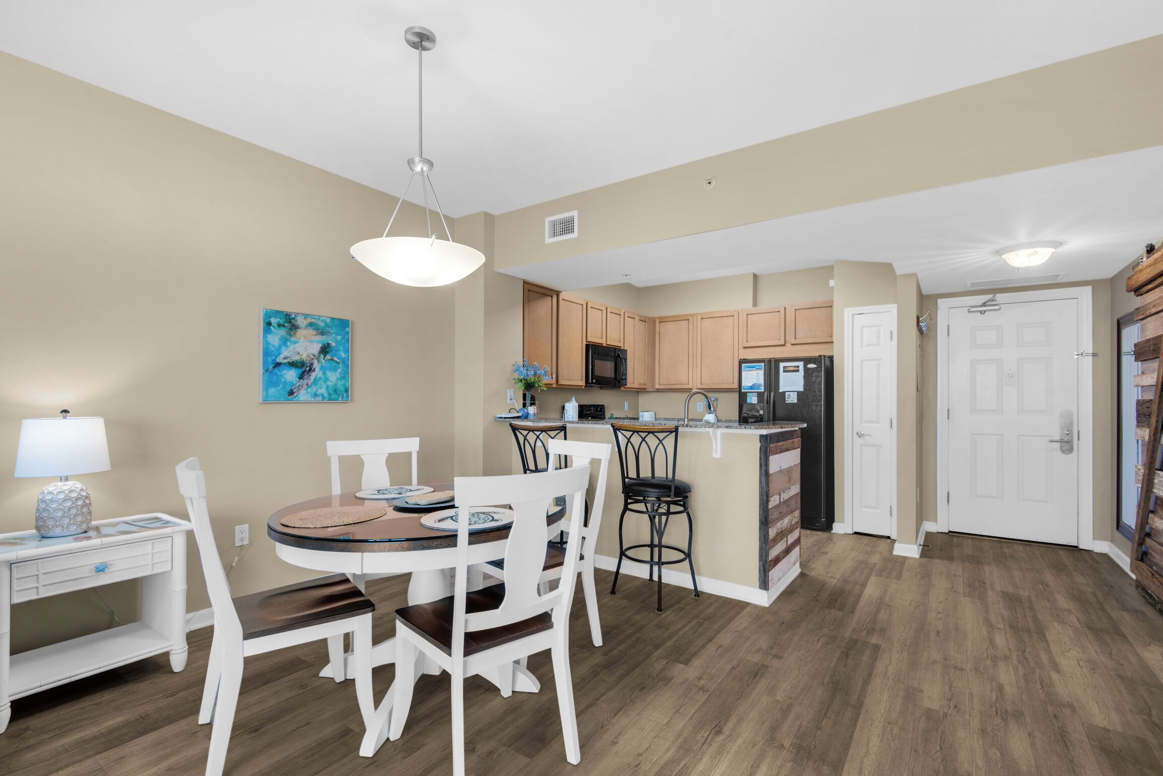 A modern kitchen with wooden cabinets, a central island, and a dining area with white chairs and a round table.