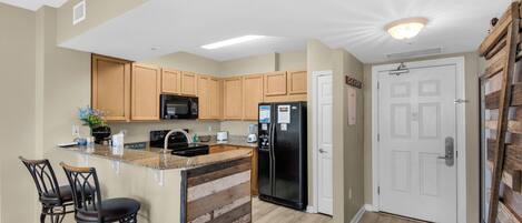 A kitchen with wooden cabinets, a black refrigerator, and a built-in island with bar stools.