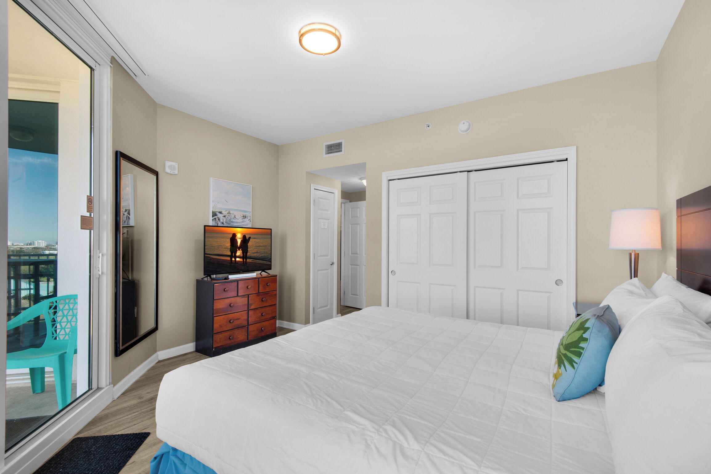A hotel room with a large bed, a dresser, a television, and a sliding glass door leading to a balcony.