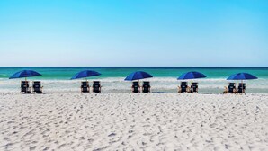 Ein Strand mit fünf Reihen von Liegestühlen und Sonnenschirmen, der zum Meer hin ausgerichtet ist.