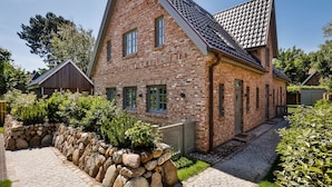 Een klassiek bakstenen huis met een steile puntige dak en een stenen muur ervoor, en een bestrate oprit.