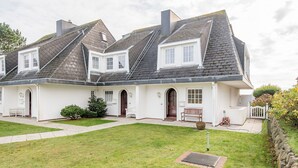 A white two-story house with a sloped roof, a front porch with a bench, and a small garden area.