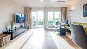 A spacious living room with a large TV, a sofa, a coffee table, and a dining area.