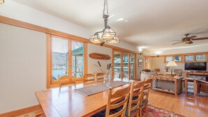 A spacious dining area with a wooden table and chairs, a chandelier, and a view of the outdoors. - Cozy Lakefront Escape w/ Sauna, Swim Spa & Views (McHenry)