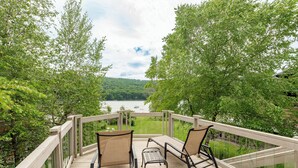 A deck with two chairs and a table overlooking a river and forest. - Cozy Lakefront Escape w/ Sauna, Swim Spa & Views (McHenry)