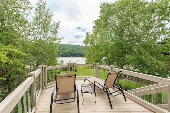 A deck with two chairs and a table overlooking a river and forest.