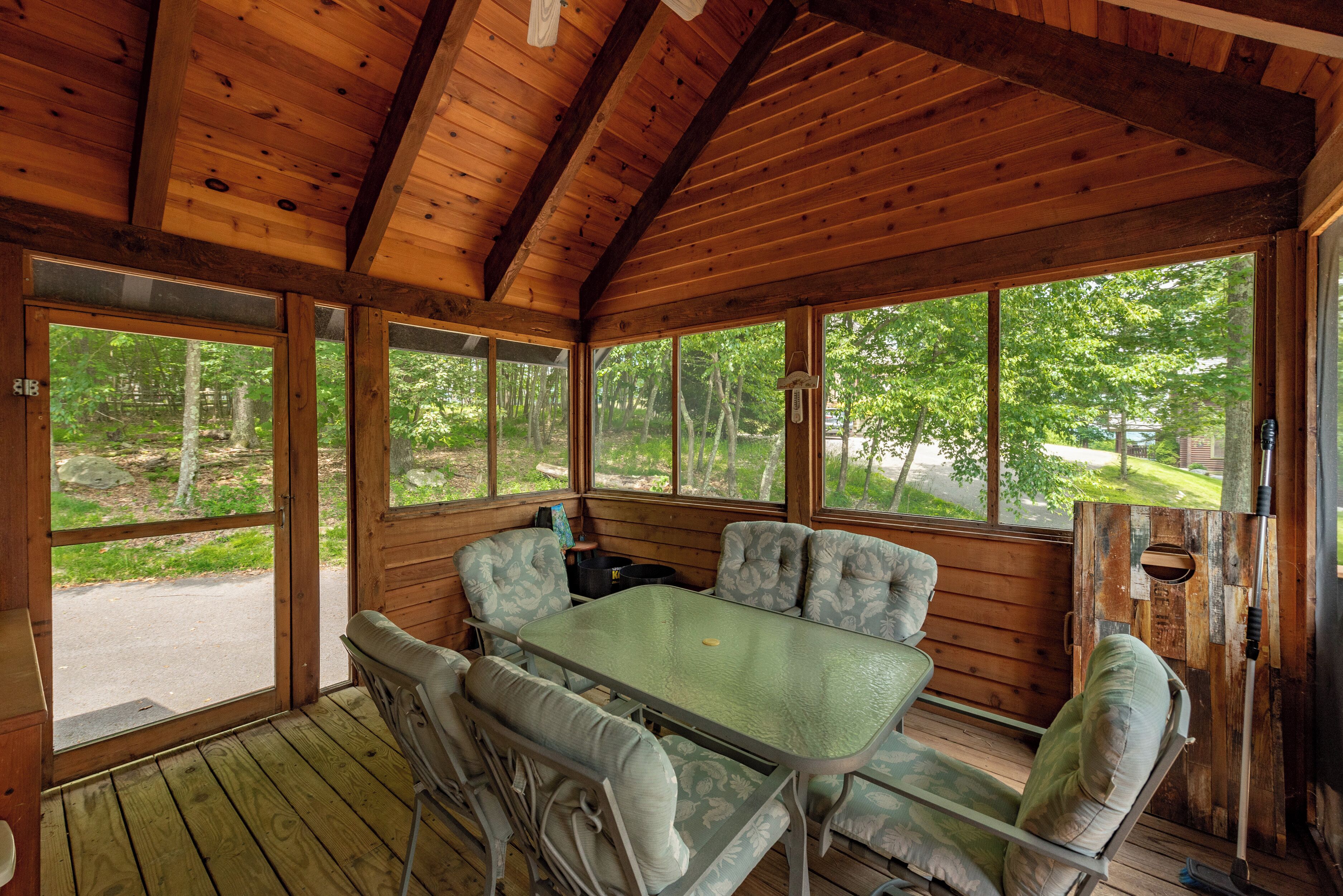 A wooden cabin with a dining table and chairs, large windows, and a view of the forest.