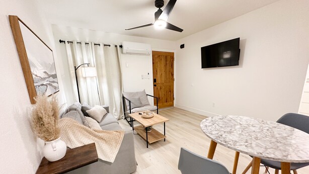 A modern living room with a grey sofa, a wooden coffee table, and a marble dining table with chairs. A ceiling fan and a flat-screen TV are mounted on the wall. - New & updated 2-bedroom 1 bathroom apt. Near Modesto 1mile from HWY 99 (Salida)