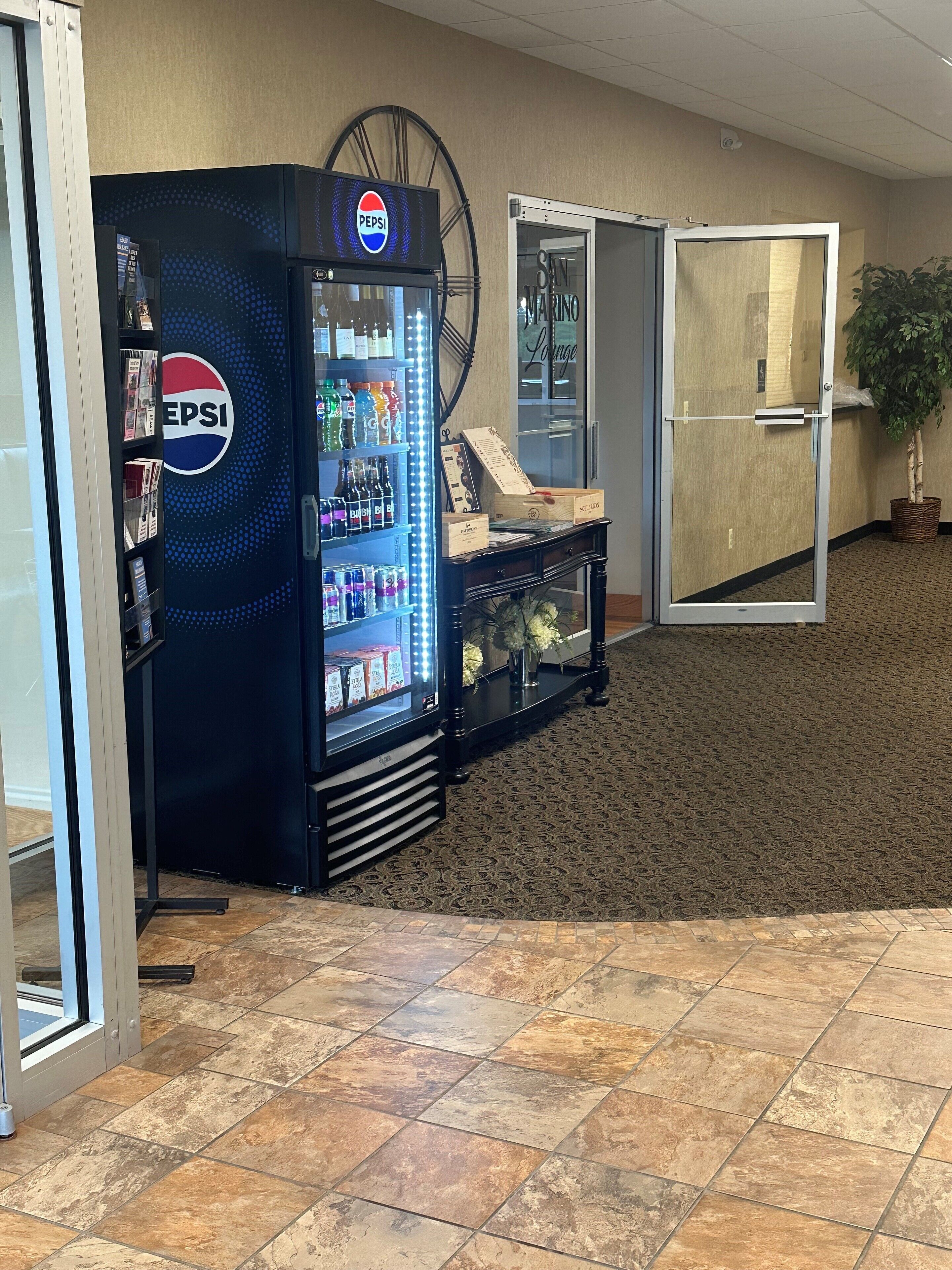 Una macchina distributrice con Pepsi, una porta in vetro e una pianta in vaso.