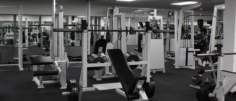 A gym with various weightlifting equipment, mirrors, and a black rubber floor.