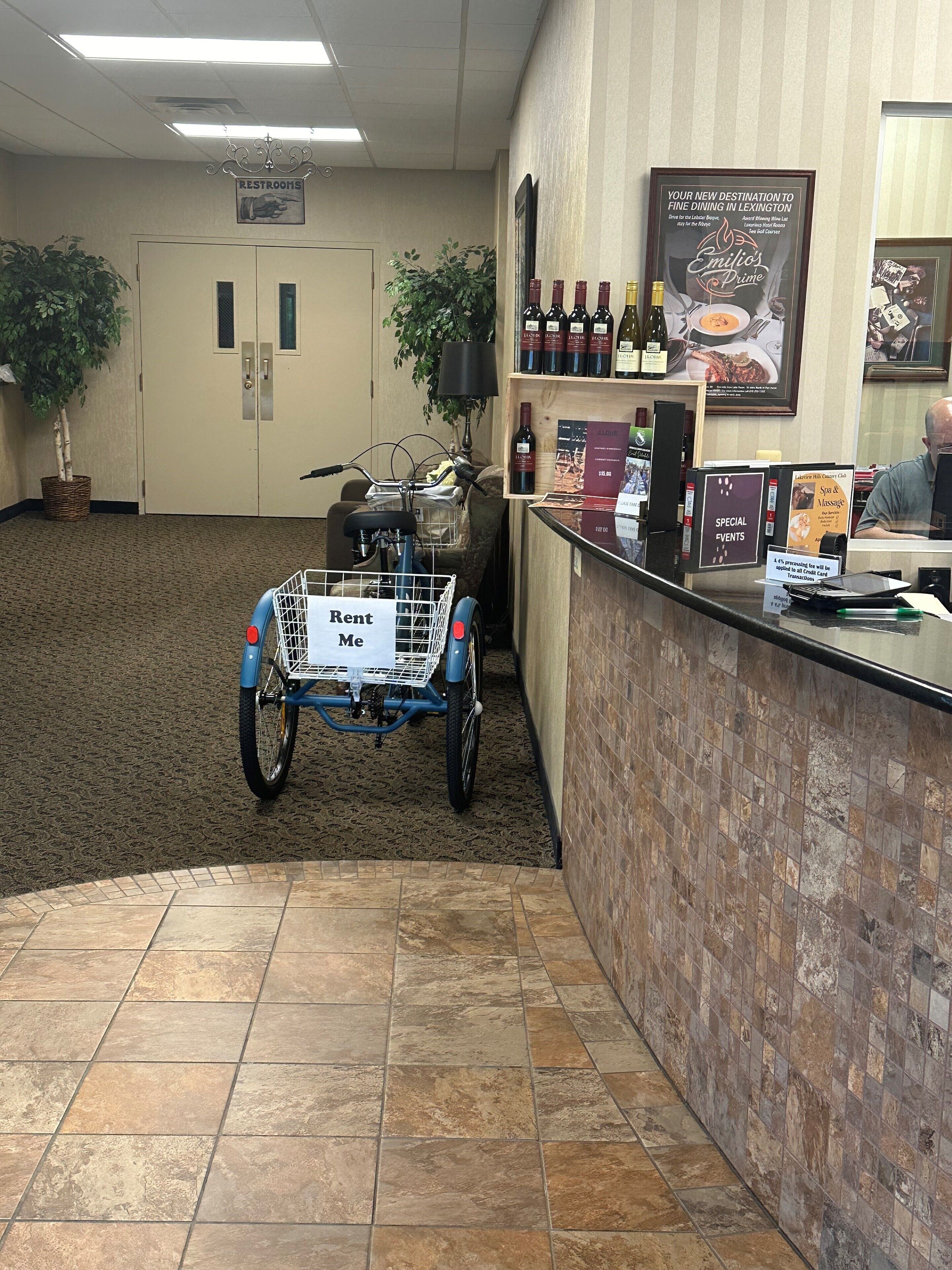 Een hotel lobby met een fietsverhuurservice, een receptiebalie en een bord voor een restaurant.