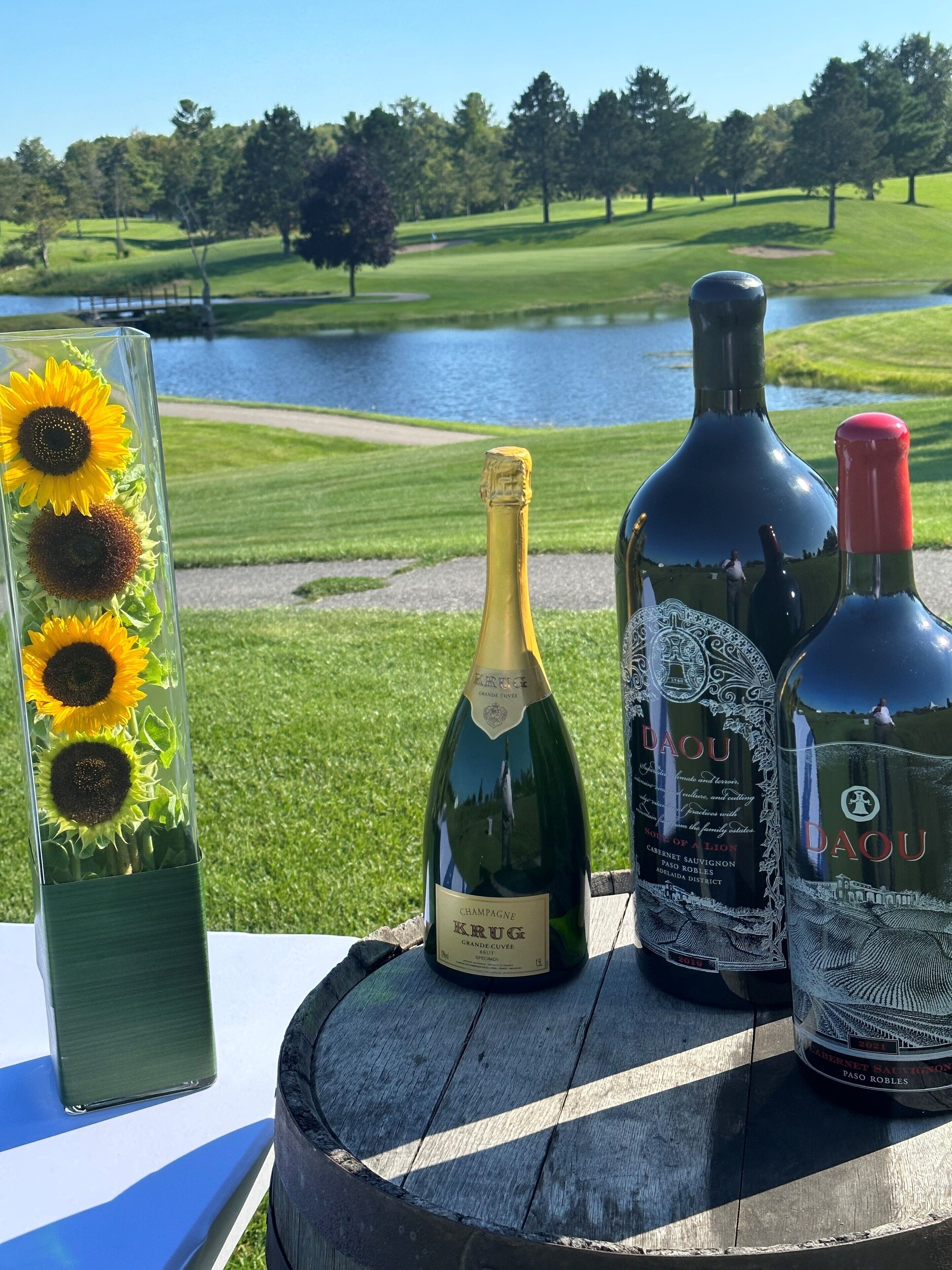 A table with three bottles of wine and a vase with sunflowers.