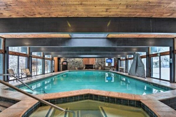 An indoor swimming pool with a wooden ceiling, stone walls, and large windows. - Shanty Creek Penthouse - on the resort! (Bellaire)