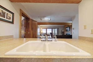 A bathroom with a large sink, wooden ceiling beams, and a framed picture on the wall.