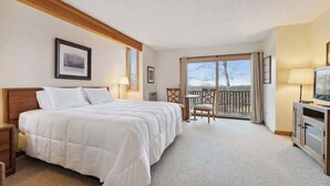 A hotel room with a large bed, a desk, a chair, a television, and a balcony with a view. - Shanty Creek Condo - on the resort! (Bellaire)