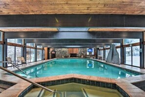 An indoor swimming pool with a wooden ceiling, stone walls, and large windows.