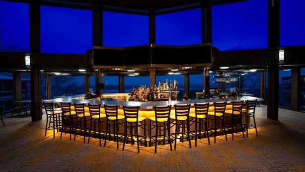 A bar area with a central island and multiple chairs, large windows, and a view outside. - Shanty Creek Condo - on the resort! (Bellaire)