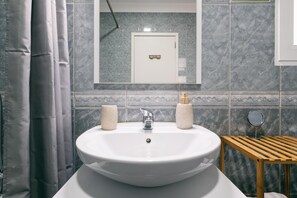 Un baño con un lavamanos blanco, dos dispensadores de jabón, un espejo y un taburete de madera.