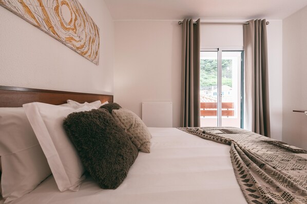 A hotel room with a large bed, a headboard, a window with curtains, and a wall with a geometric artwork.