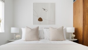 Moderni hotellihuone, jossa on suuri sänky, kaksi yöpöytää valaisimineen ja puupaneloitu seinä.