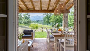 An outdoor patio with wicker furniture, a stone table, and a view of a green landscape with trees and mountains. - Anticiana 8, Emma Villas (Lucca)
