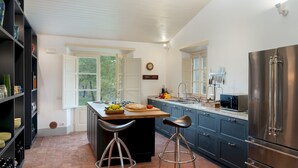 A modern kitchen with a central island, bar stools, a stainless steel refrigerator, and a window with a view of trees. - Anticiana 8, Emma Villas (Lucca)