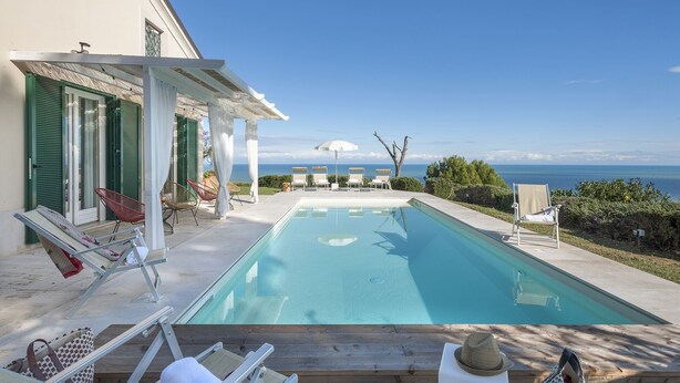 A pool with lounge chairs and umbrellas, a view of the sea, and a building with green shutters. - Villa Lucente 6+2, Emma Villas (Silvi Paese)