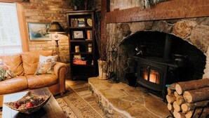A cozy living room with a stone fireplace, a leather sofa, a bookshelf, and a rustic decor. - Stilly River Haus - Hot tub - Sauna - Fireplace (Granite Falls)