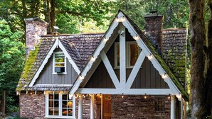 A rustic cabin with a steeply pitched roof, a chimney, and a porch with string lights. - Stilly River Haus - Hot tub - Sauna - Fireplace (Granite Falls)