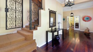 Un escalier orné d’une rampe en métal décorative, une console sur laquelle est posé un vase, un miroir et un plancher en bois.