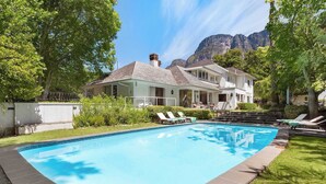 Une piscine avec des chaises longues, une maison dotée d’un balcon et une montagne en arrière-plan.