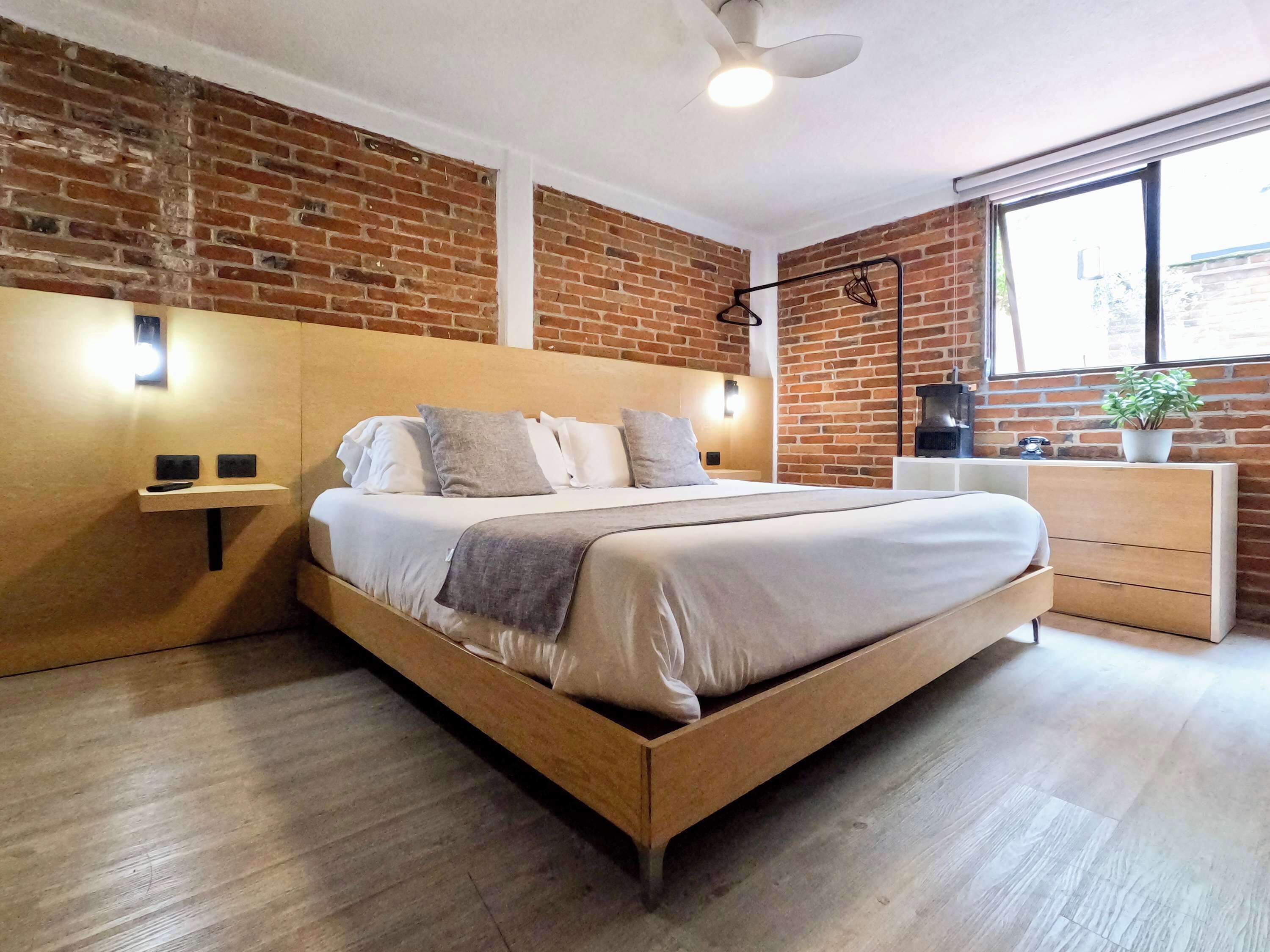 Un dormitorio moderno con pared de ladrillo, cama de madera, mesitas de noche, cómoda y una ventana.