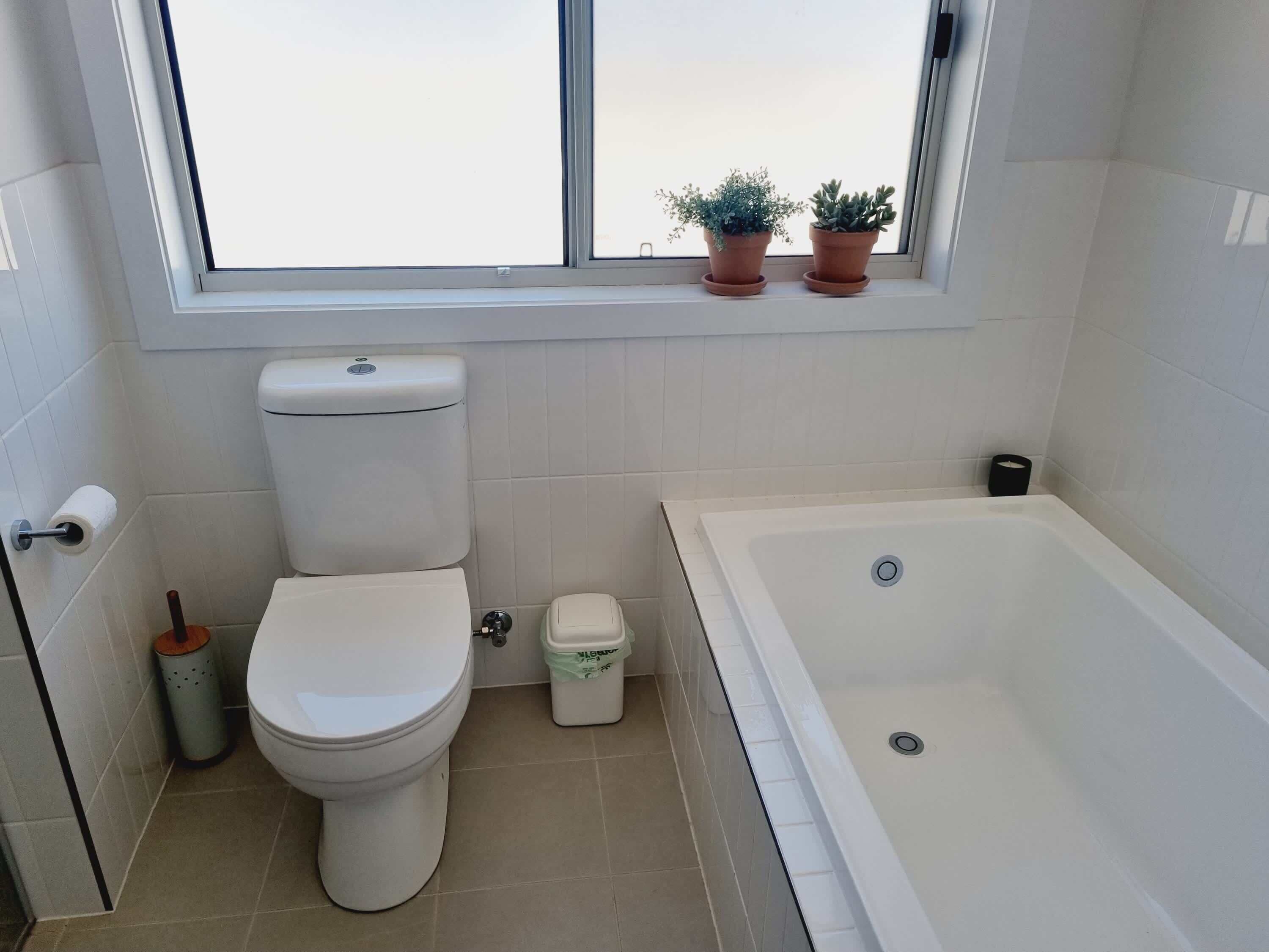Et badeværelse med toilet, bidet og badekar. Der står to plantede planter på vindueskarmen.
