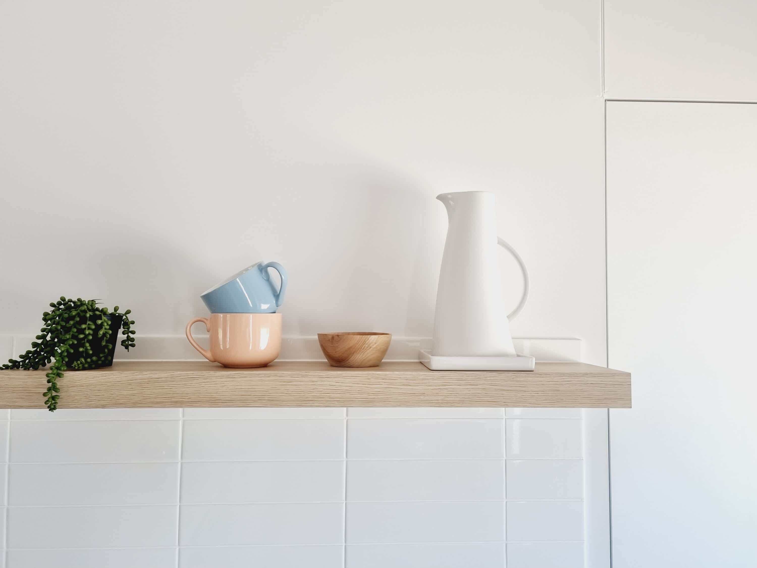 A kitchen counter with a potted plant, a stack of cups, a wooden bowl, and a white pitcher.