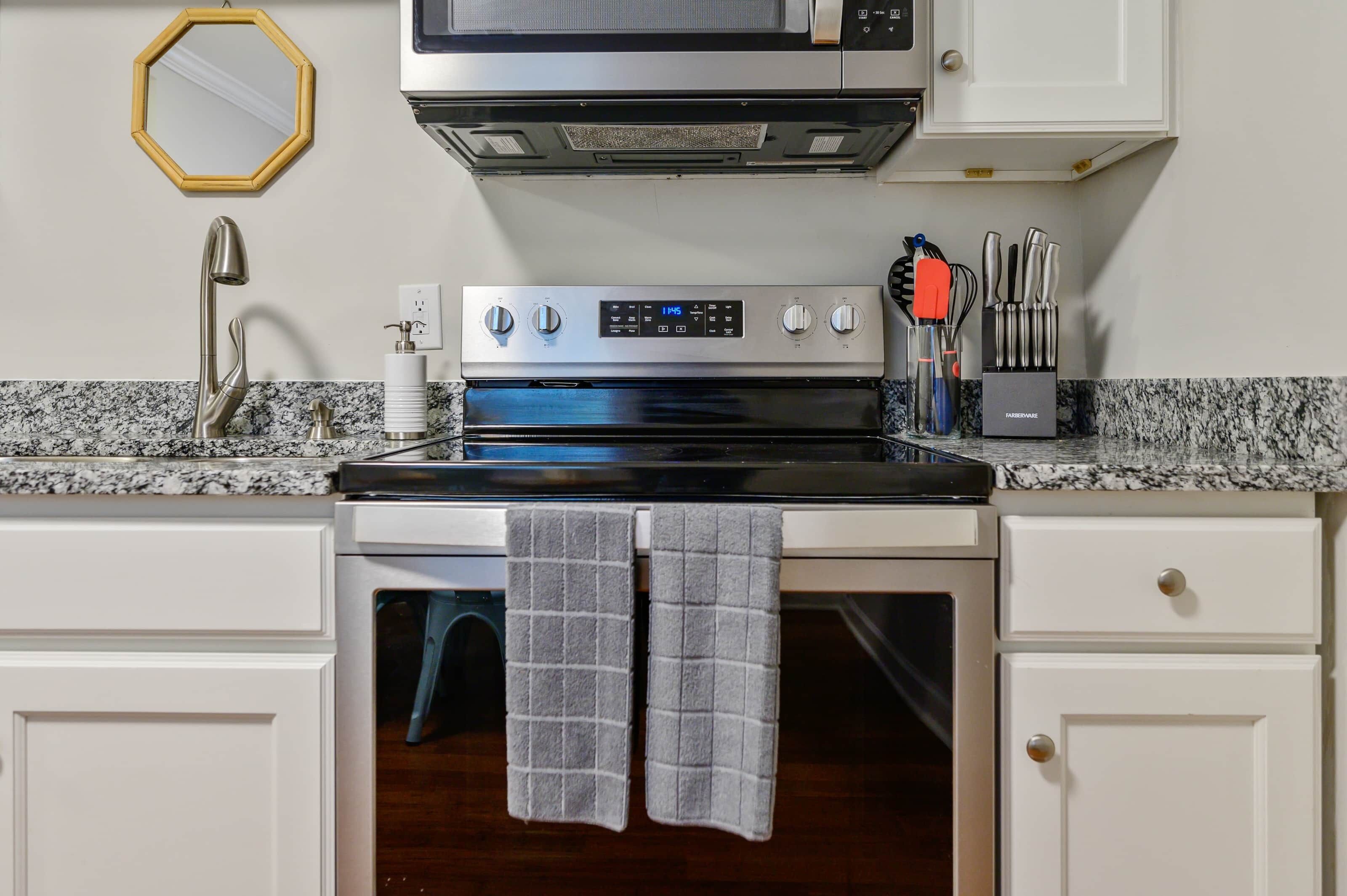 A kitchen with a stainless steel oven, a microwave, and a sink with a modern faucet. There are two towels hanging on the oven door.