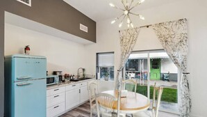 A compact kitchen with a blue refrigerator, white cabinets, and a dining area with a wooden table and white chairs. - The Gregory: 2 Bed/1 Bath Guesthouse (Phoenix)