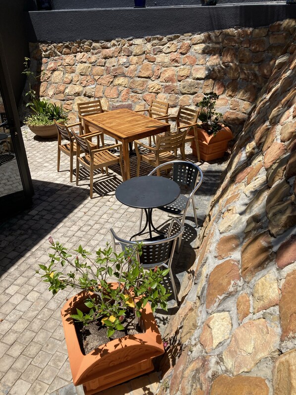 Eine Terrassengaststätte mit Holztischen und -stühlen, umgeben von Steinmauern und Blumentöpfen.