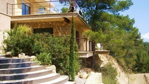 Ein zweigeschossiges Steinhaus mit Balkon, umgeben von Bäumen und einem Kiesweg.