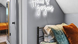 Une chambre à coucher avec un lit, un néon accroché au mur et une porte donnant sur une autre pièce.