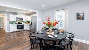 Une cuisine moderne avec des meubles blancs, des appareils en acier inoxydable et un coin repas comprenant une table ronde et des chaises noires.