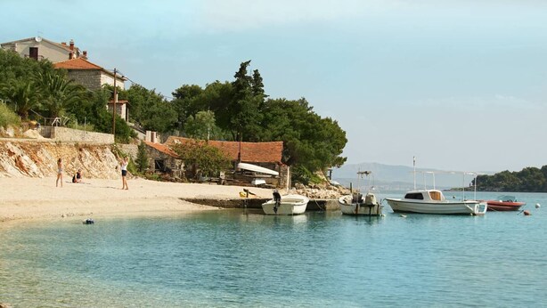 A coastal area with boats docked near the shore, a sandy beach, and a building with a red roof. - Villa del Mar - LUXURY VILLA with POOL & GARDEN (Rogac, Solta)