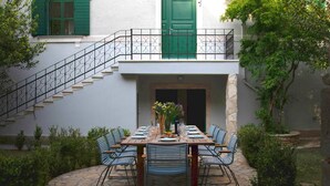 A stone patio with a wooden table set for dining, surrounded by blue chairs, and a staircase with green doors. - Villa del Mar - LUXURY VILLA with POOL & GARDEN (Rogac, Solta)