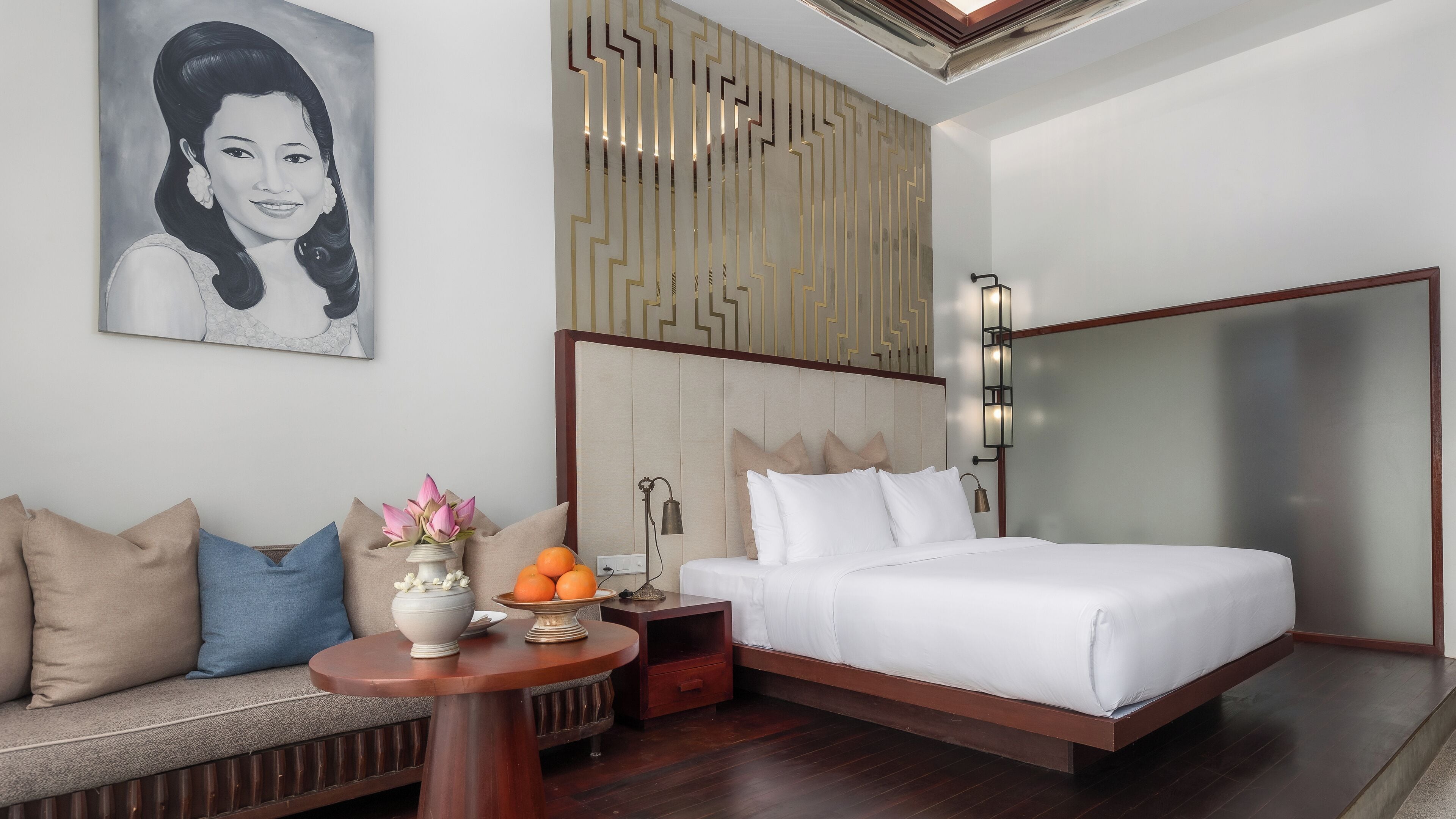 A hotel room with a bed, a sofa, a nightstand, a vase with flowers, and a wall-mounted light fixture.