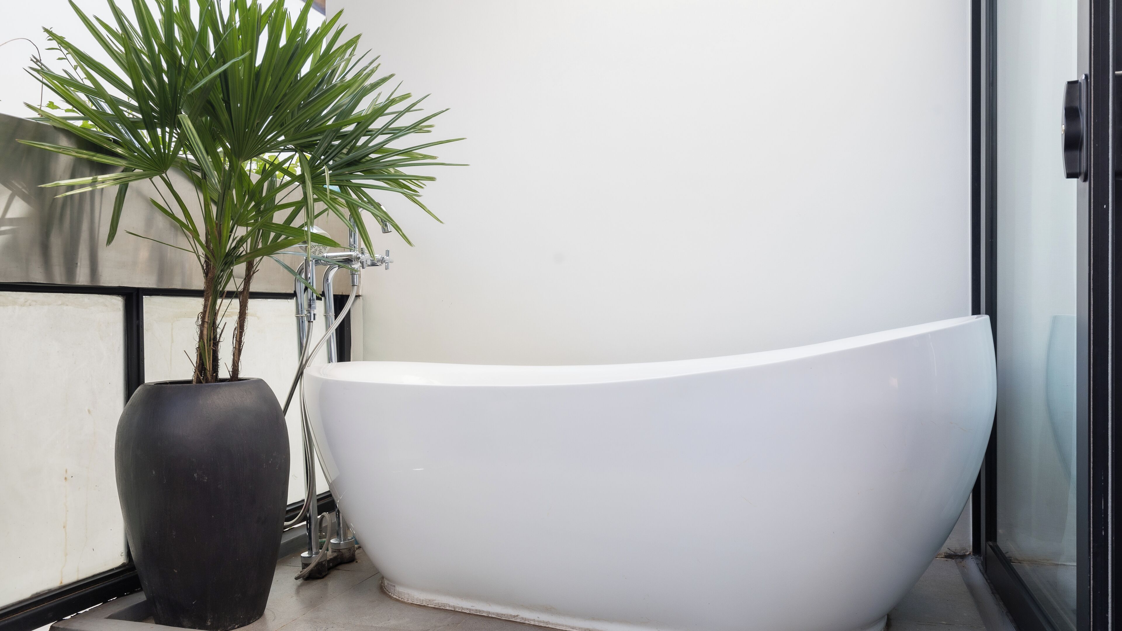 A modern bathroom with a freestanding bathtub, a potted plant, and a visible shower area.