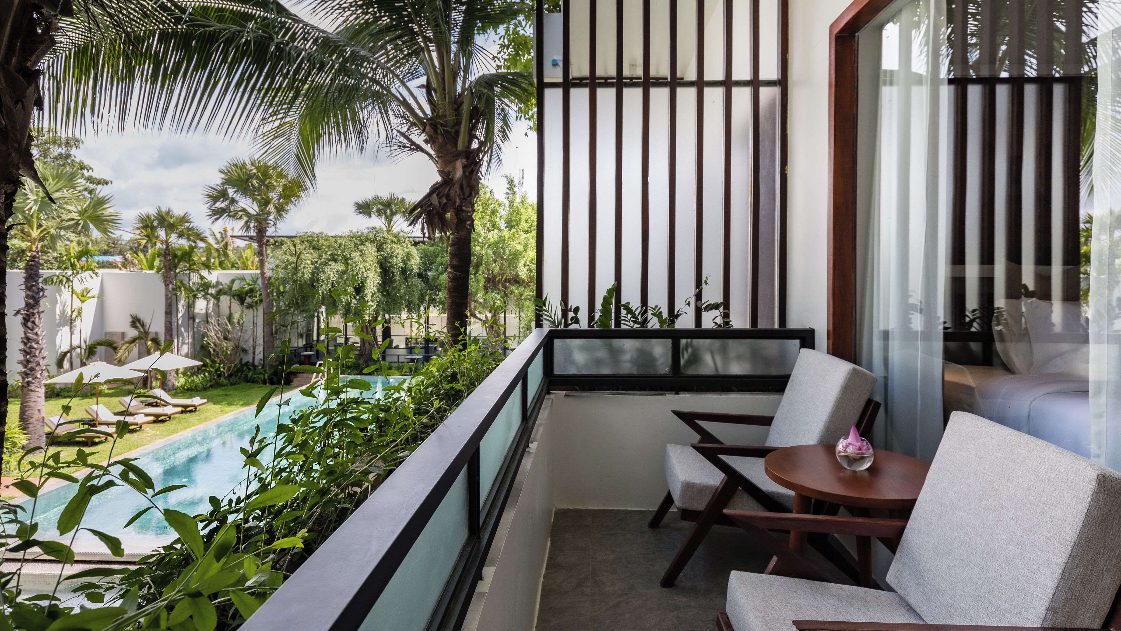 A balcony with a pool, lounge chairs, and a view of a garden.