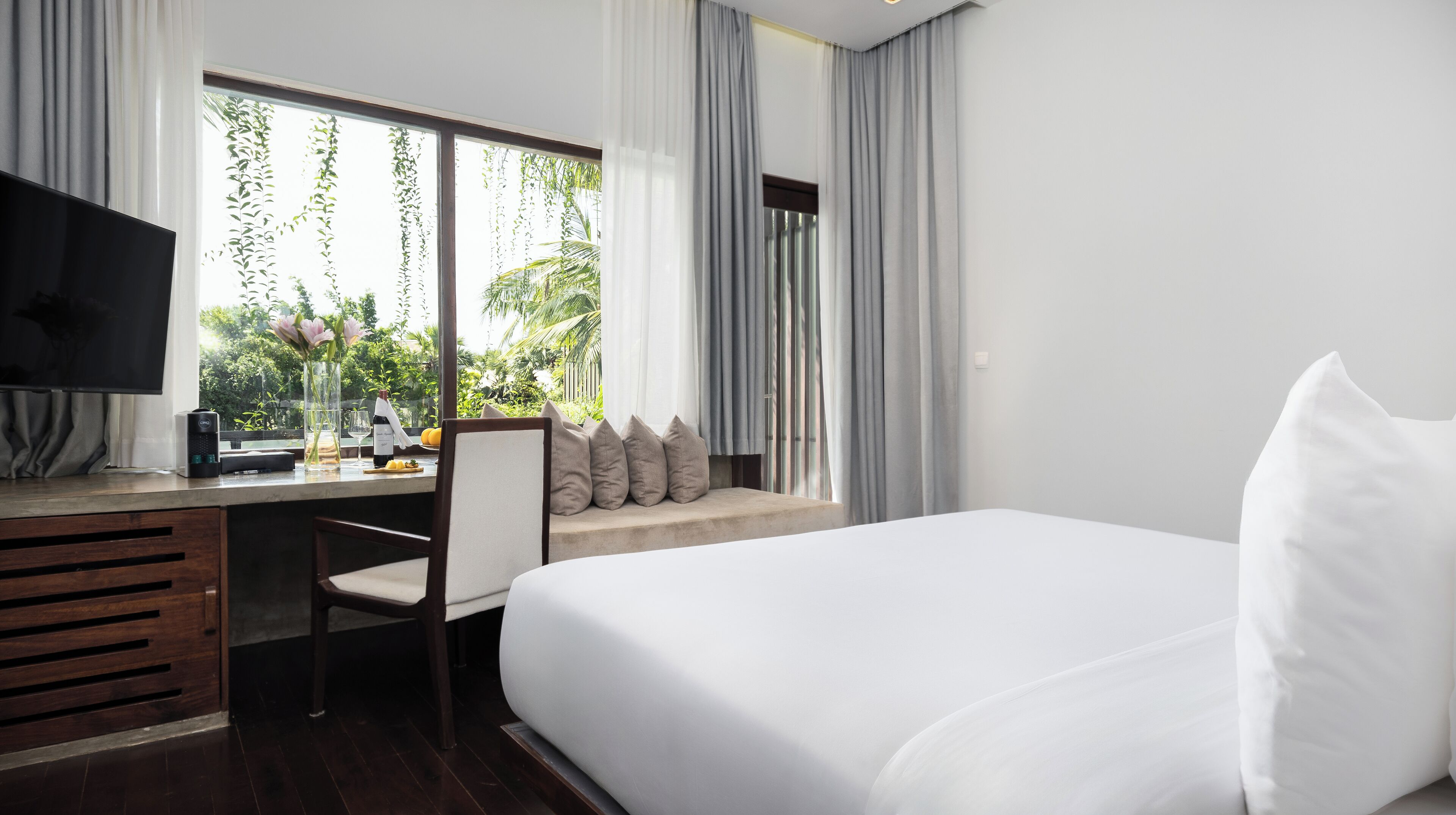 Habitación de hotel con cama, escritorio, silla, televisor y ventana con cortinas.