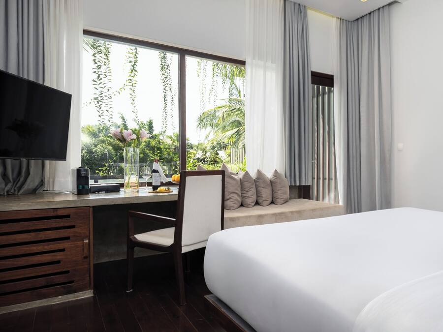 Habitación de hotel con cama, escritorio, silla, televisor y ventana con cortinas.