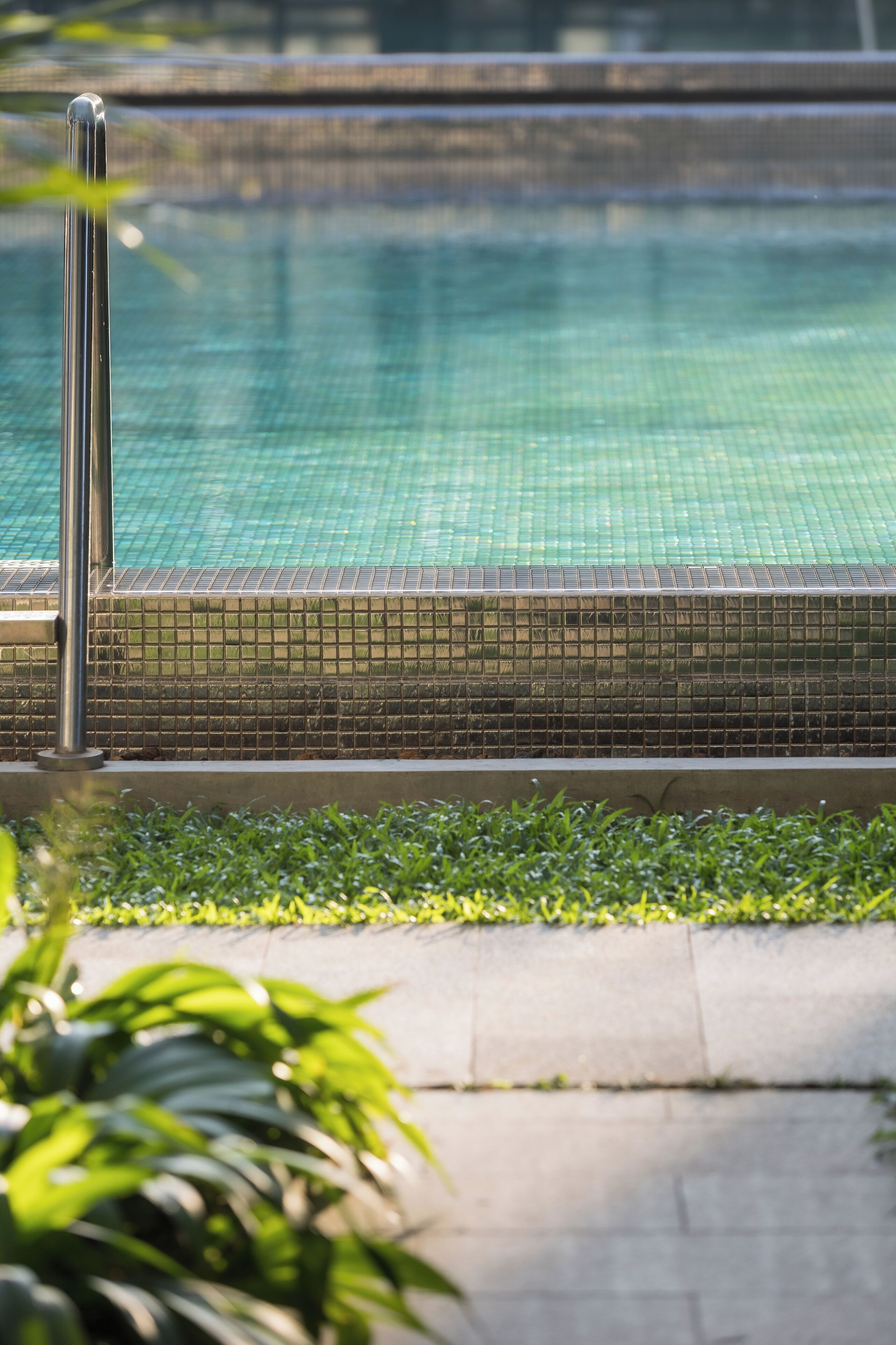 Una piscina con borde de azulejos y barandilla metálica.